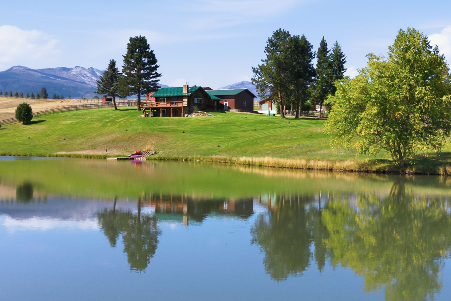 1335 Country Road homestead reflected in its pond, with pastures and mountains behind